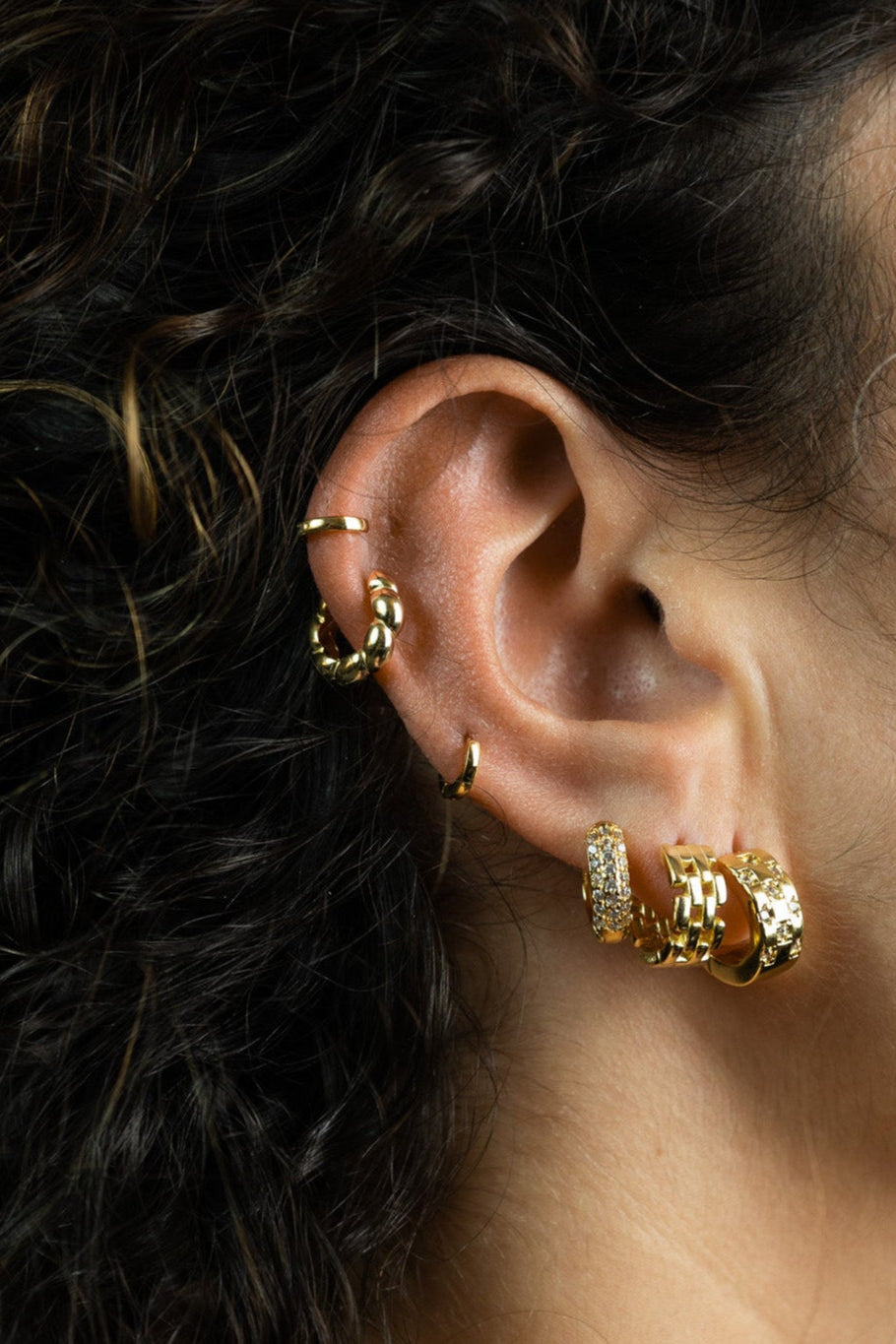 Close-up of an ear wearing gold hoop earrings and rings with a dark background