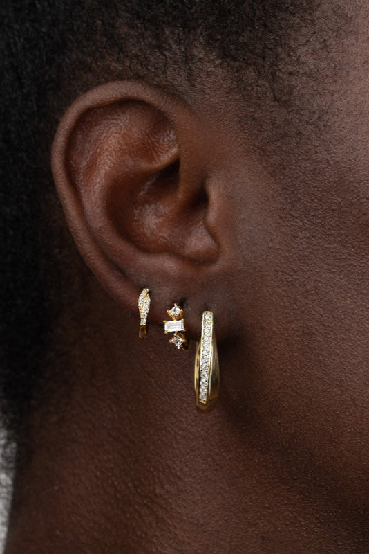 A close-up image of a woman's ear wearing a white gold-plated sterling silver hoop earring with three zirconias.