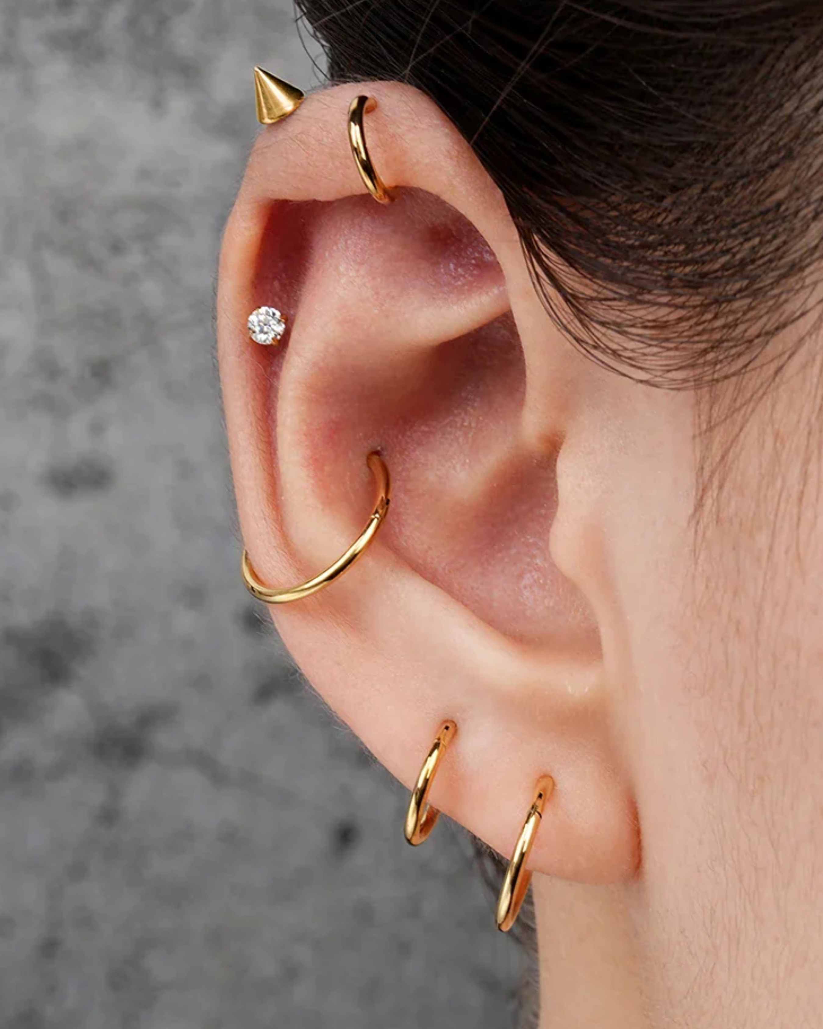 Close-up of an ear with gold earrings against a neutral background